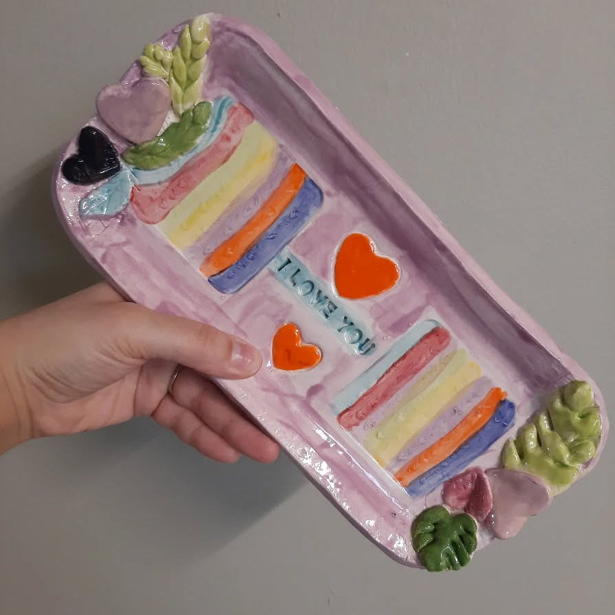 Handmade ceramic tray with colorful design held by a person against a plain background